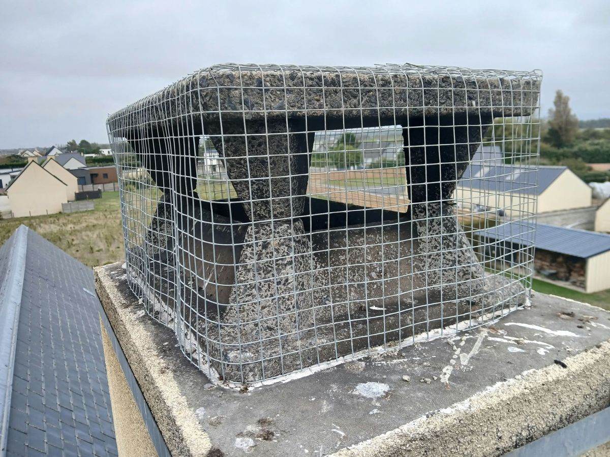 Tête de cheminée en béton entourée d'un grillage métallique anti-oiseaux, vue de face, à Créances