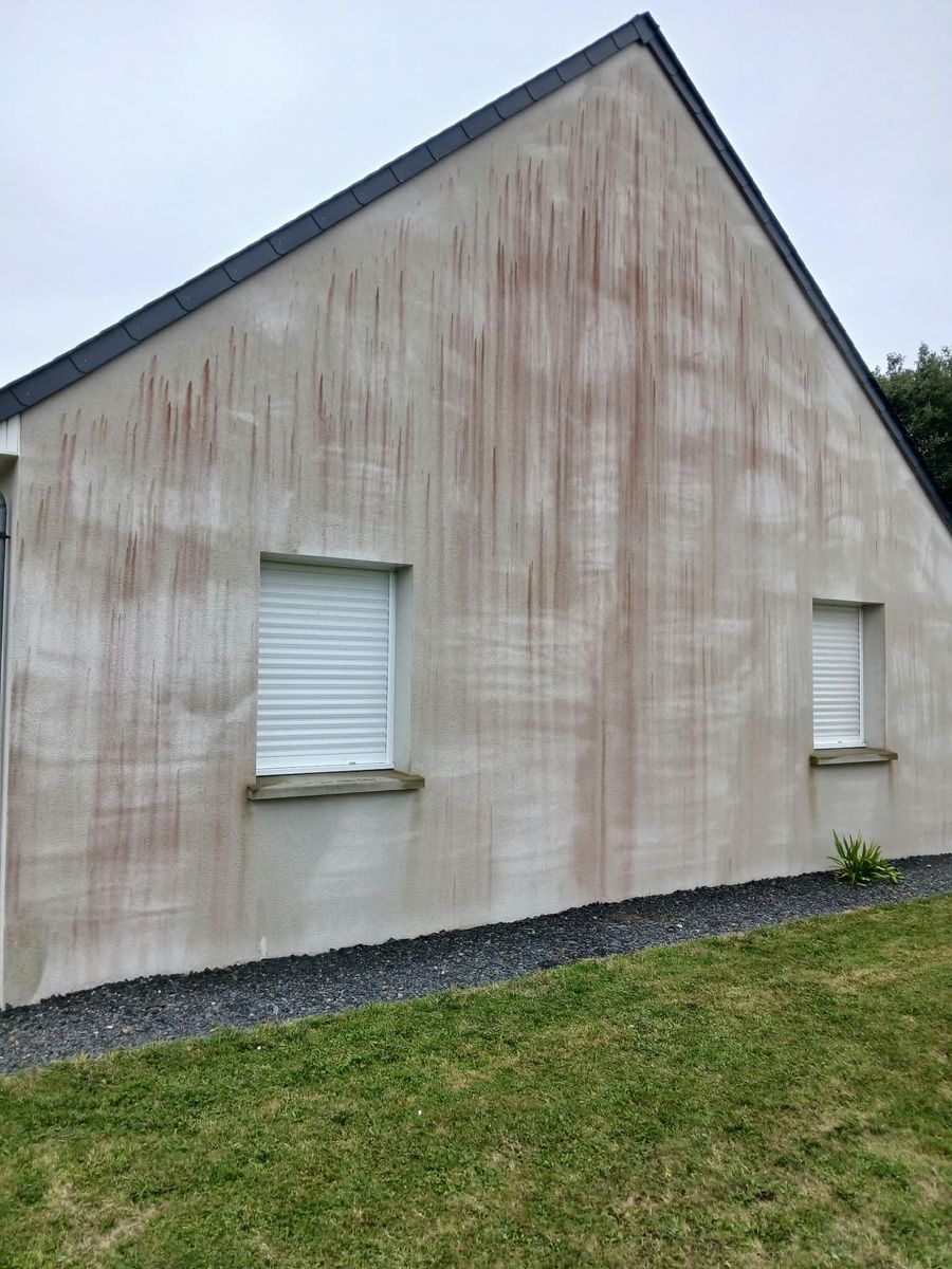Pignon de maison en enduit clair couvert de coulures rouges d'algues avant nettoyage, à Lessay